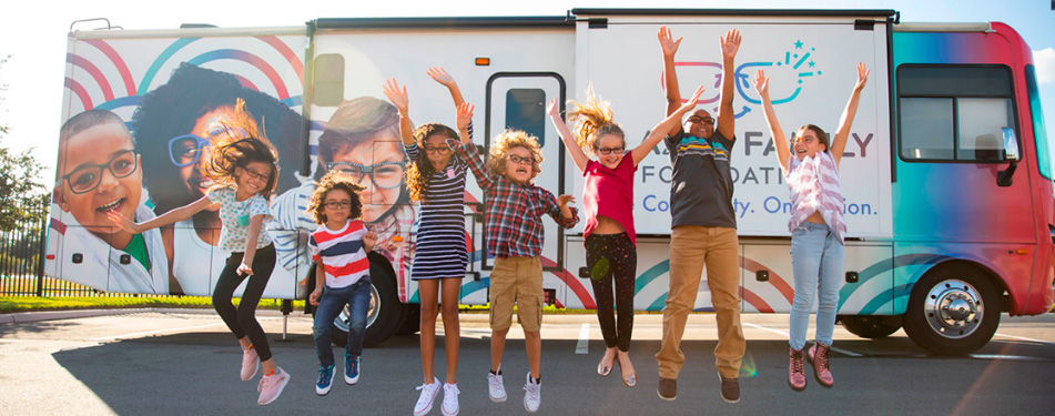 seven children jumping in the air with the mobile vision clinic bus in the background
